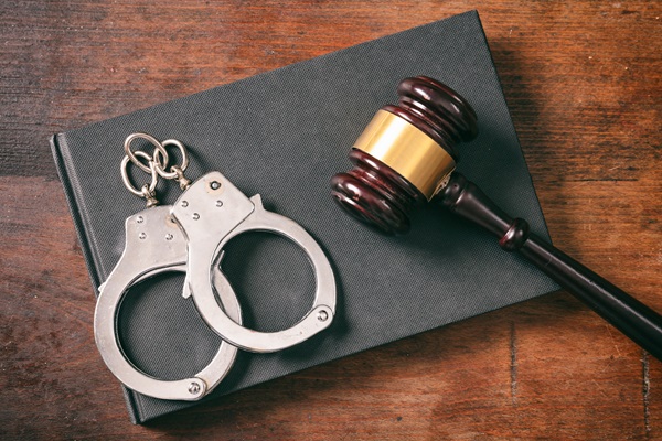A pair of silver metal handcuffs and a wooden judge’s gavel resting on a black law book, symbolizing the legal consequences of facing multiple criminal charges in Texas.
