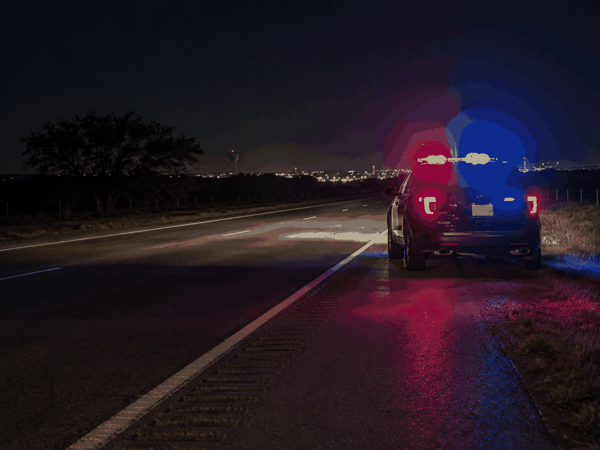 Texas police car parked along a dark highway at night with red and blue emergency lights flashing.